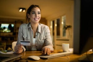uma mulher em frente a um computador com um cartão conta salário na mão