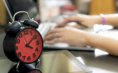 uma pessoa no computador com um despertador vermelho do lado em jornada de 44 horas semanais