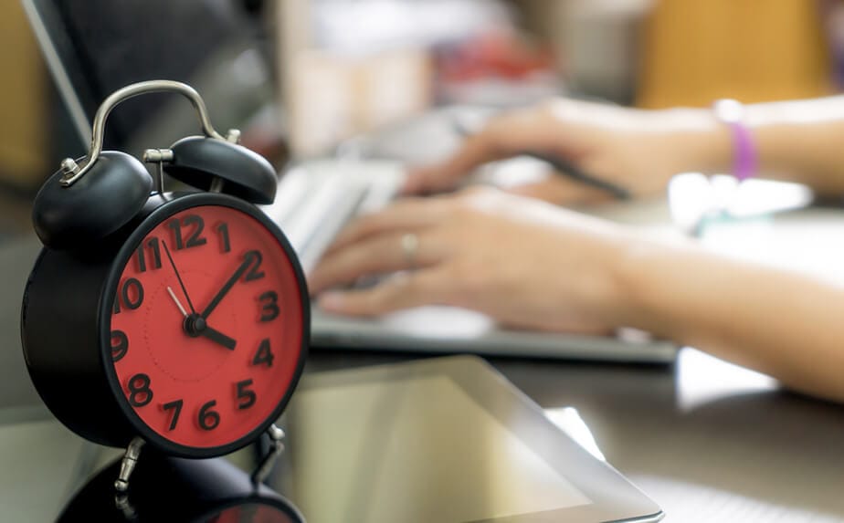 uma pessoa no computador com um despertador vermelho do lado em jornada de 44 horas semanais